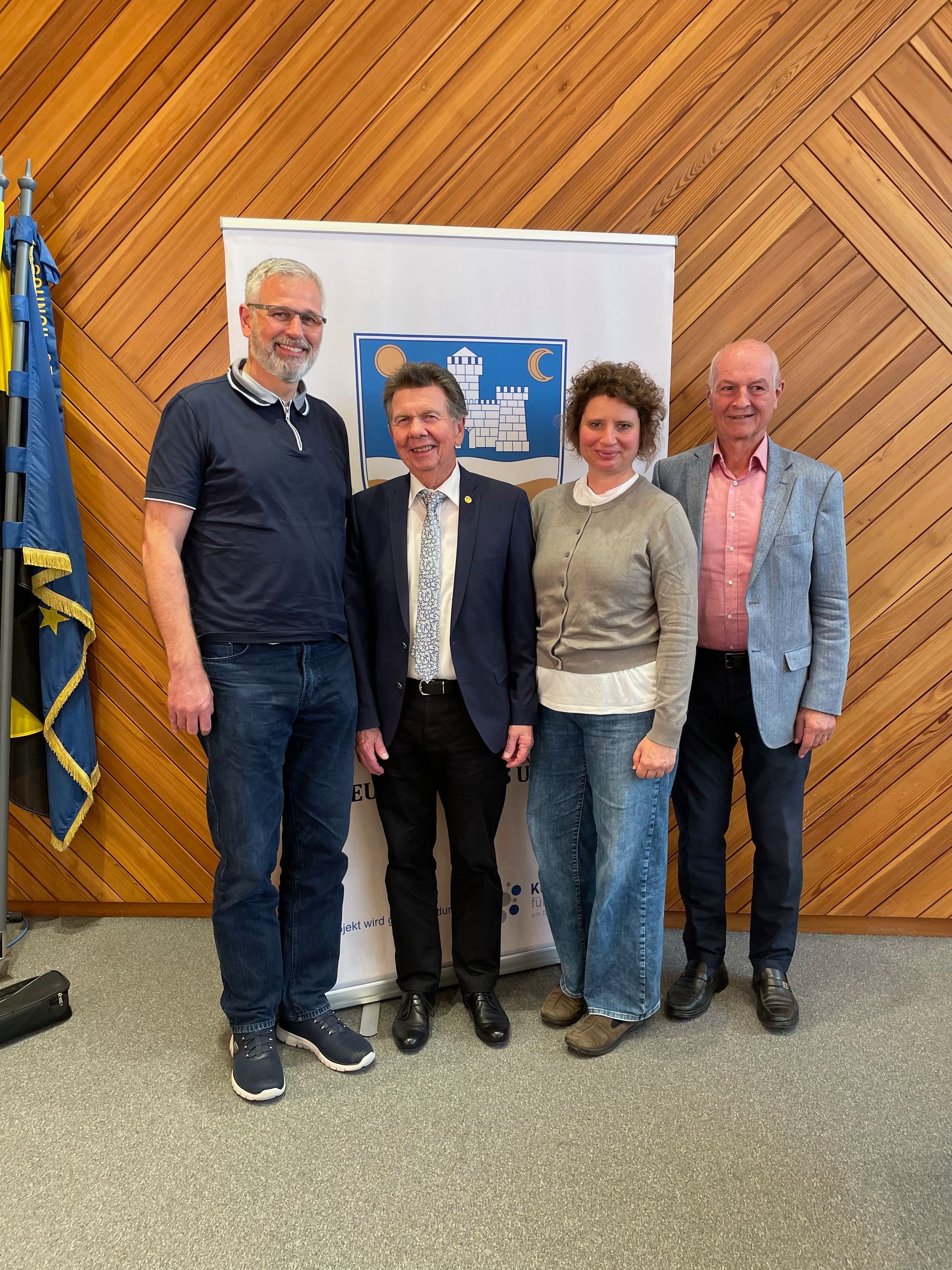 Vor dem Banner der Landsmannschaft der Deutschen aus Ungarn stehen die Vertreter des Gemeinderats Jürgen Fritz, Angela Neuburger-Schäfer und Jürgen Wöhler. In ihrer Mitte steht der bei der Tagung geehrte Erich Gscheidle. 