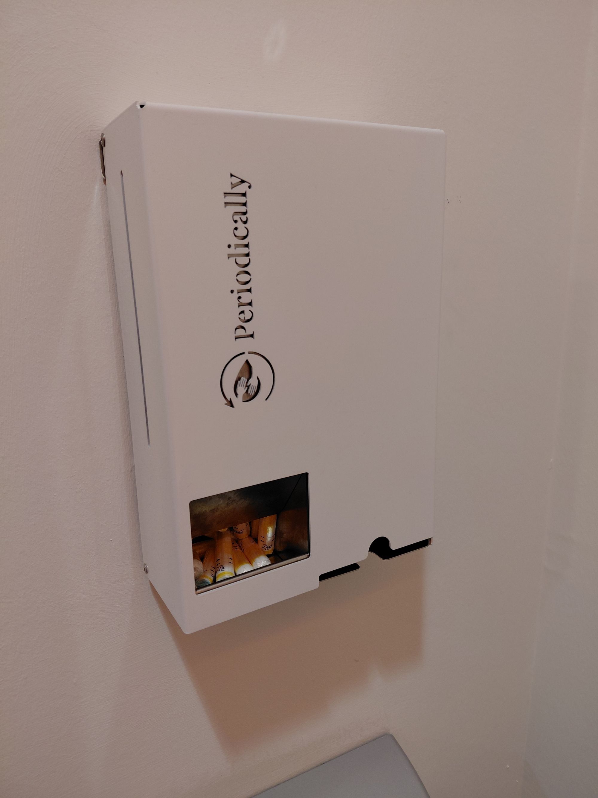 Ein länglicher weißer Kasten mit der Aufschrift "Periodically" hängt an einer Wand. 