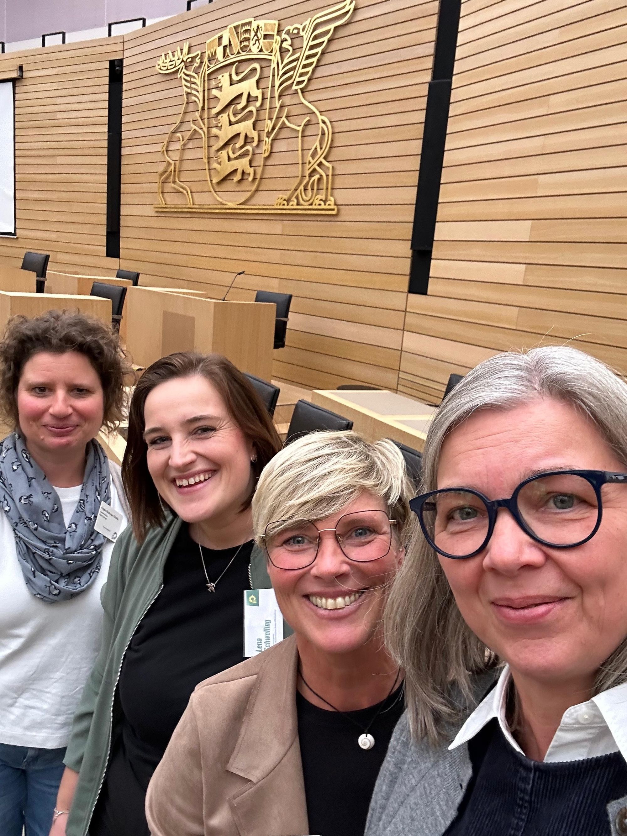 Vor der Regierungsbank des Landtages in Stuttgart stehen die vier Frauen. Es sind nur ihre Köpfe zu sehen. Über ihnen ist an der mit Holz vertäfelten Wand das große Landeswappen in Gold zu sehen. 